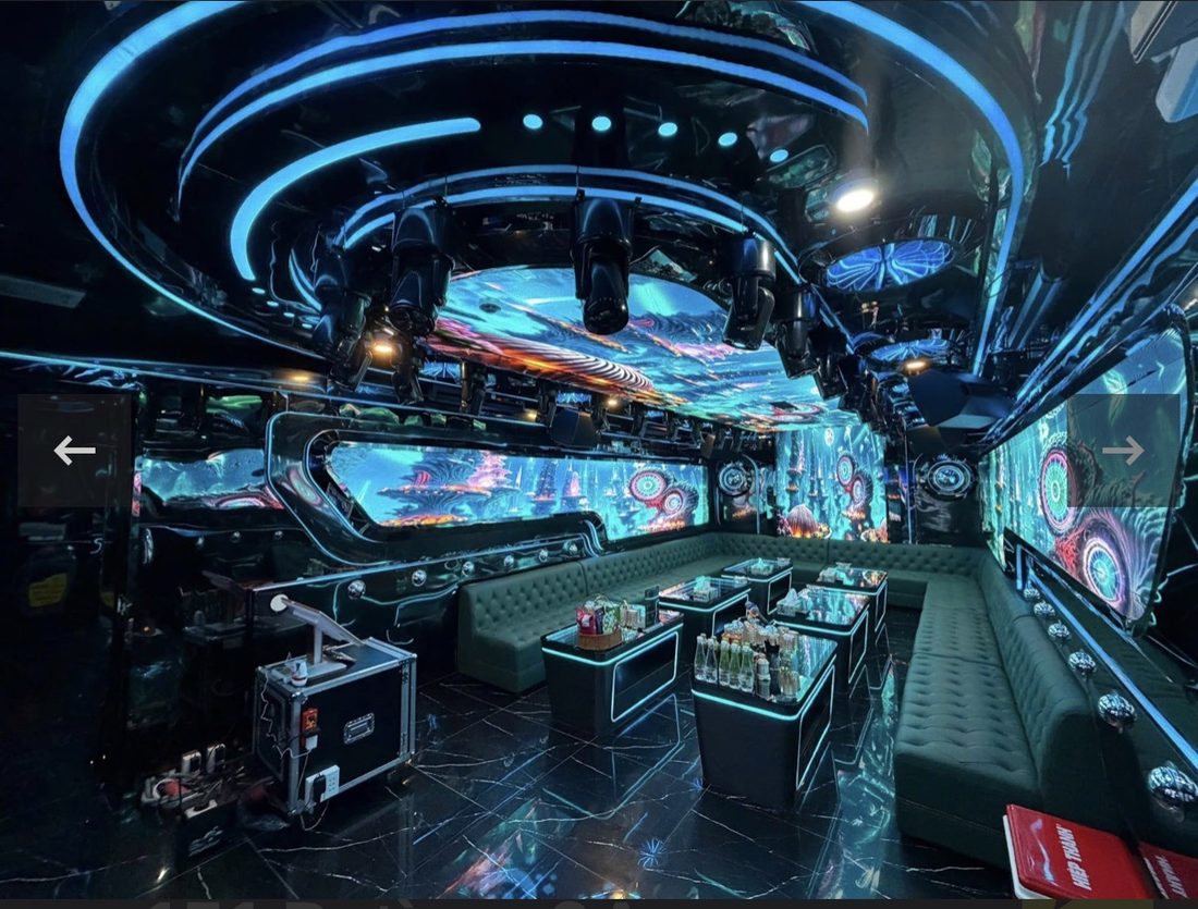 DRAGON PALACE KTV 大包廂天花同心圓藍色光環與一排搖頭燈，L 形墨綠卡座圍成大圈，角落放燈光控台機箱