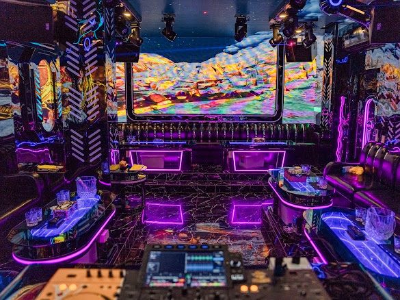 大房 DJ 艙：前景一整套 DJ 打碟控制台，正牆弧形 LED 放彩色山脈，兩側人字紋發光牆板